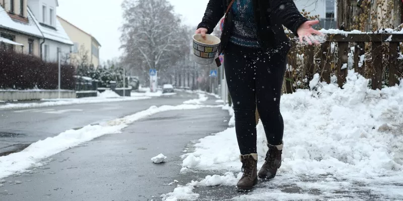 Woman throwing salt on snowy sidewalk
